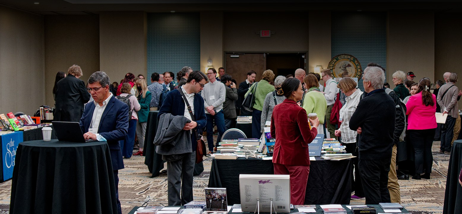 Attendees browsing books and talking at a Society for American Music conference exhibit